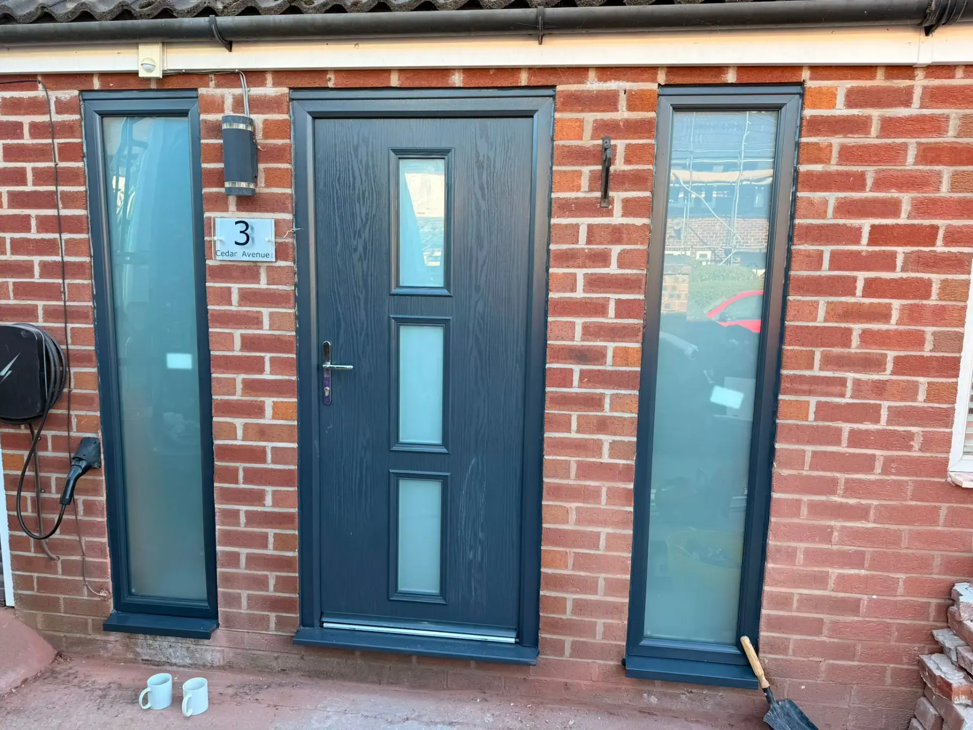 Anthracite grey composite door with full-height glazed side panels in a red brick porch