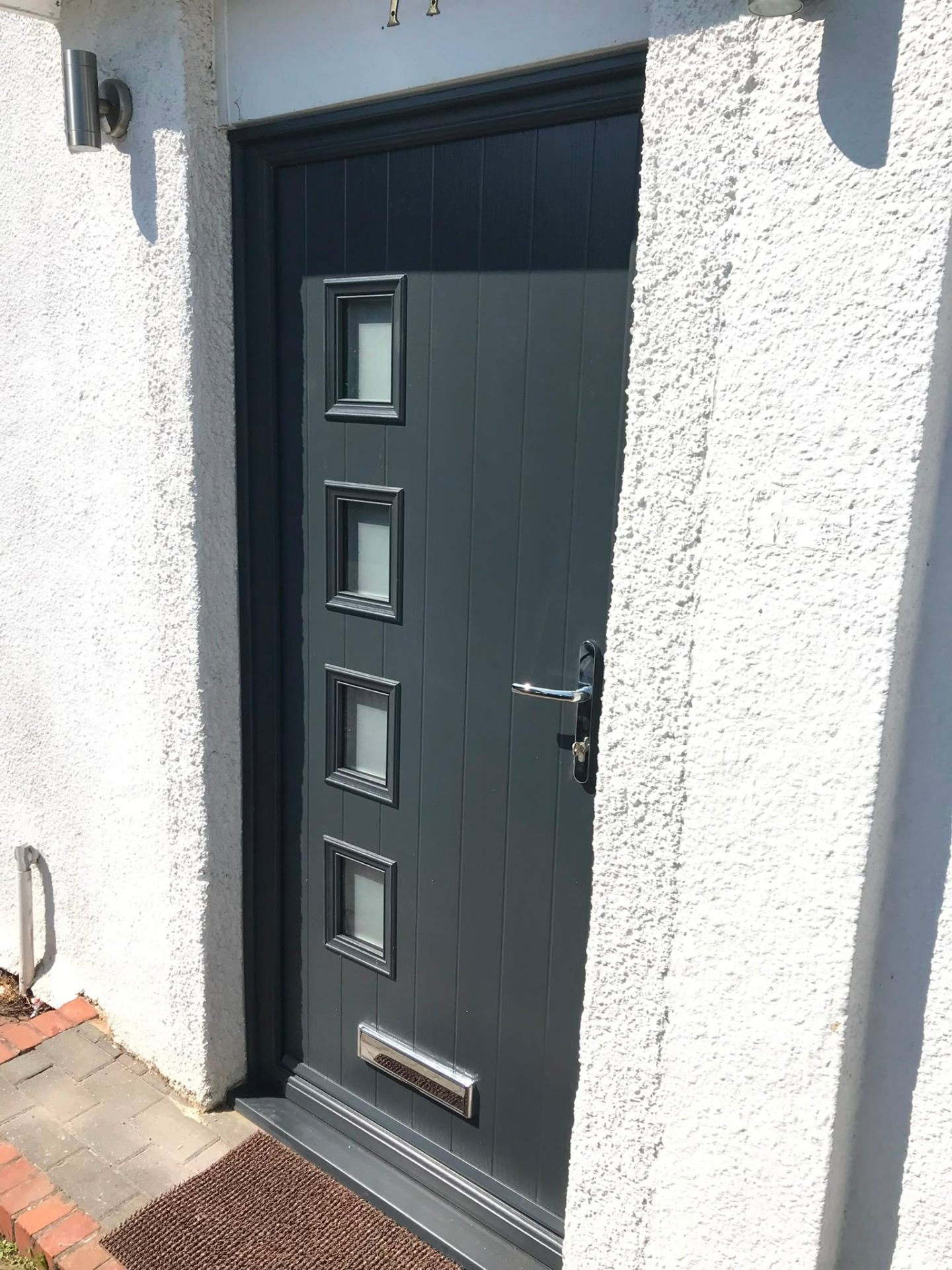 Anthracite grey composite front door with four square glazed panels on a rendered house
