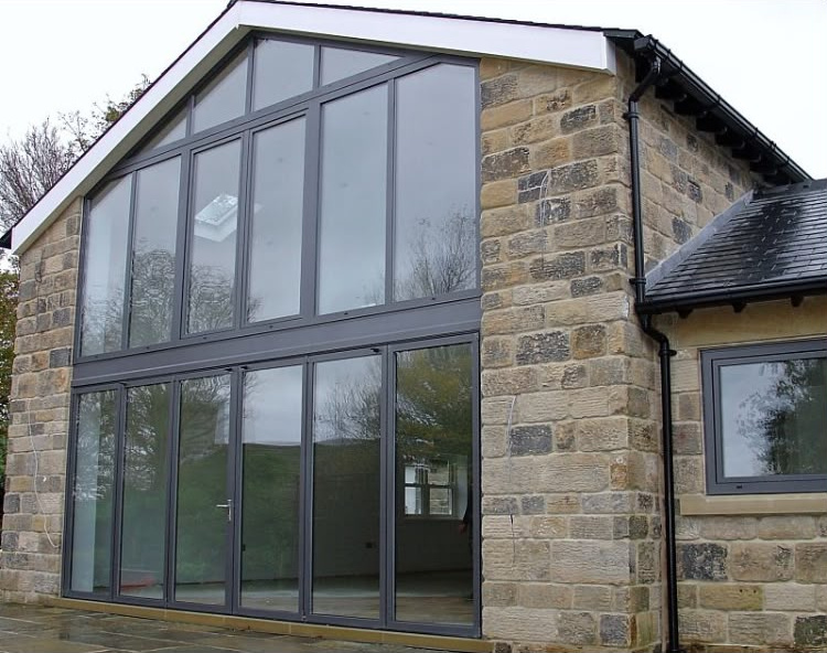 Full-height anthracite grey aluminium gable glazing and patio doors on a stone-built home